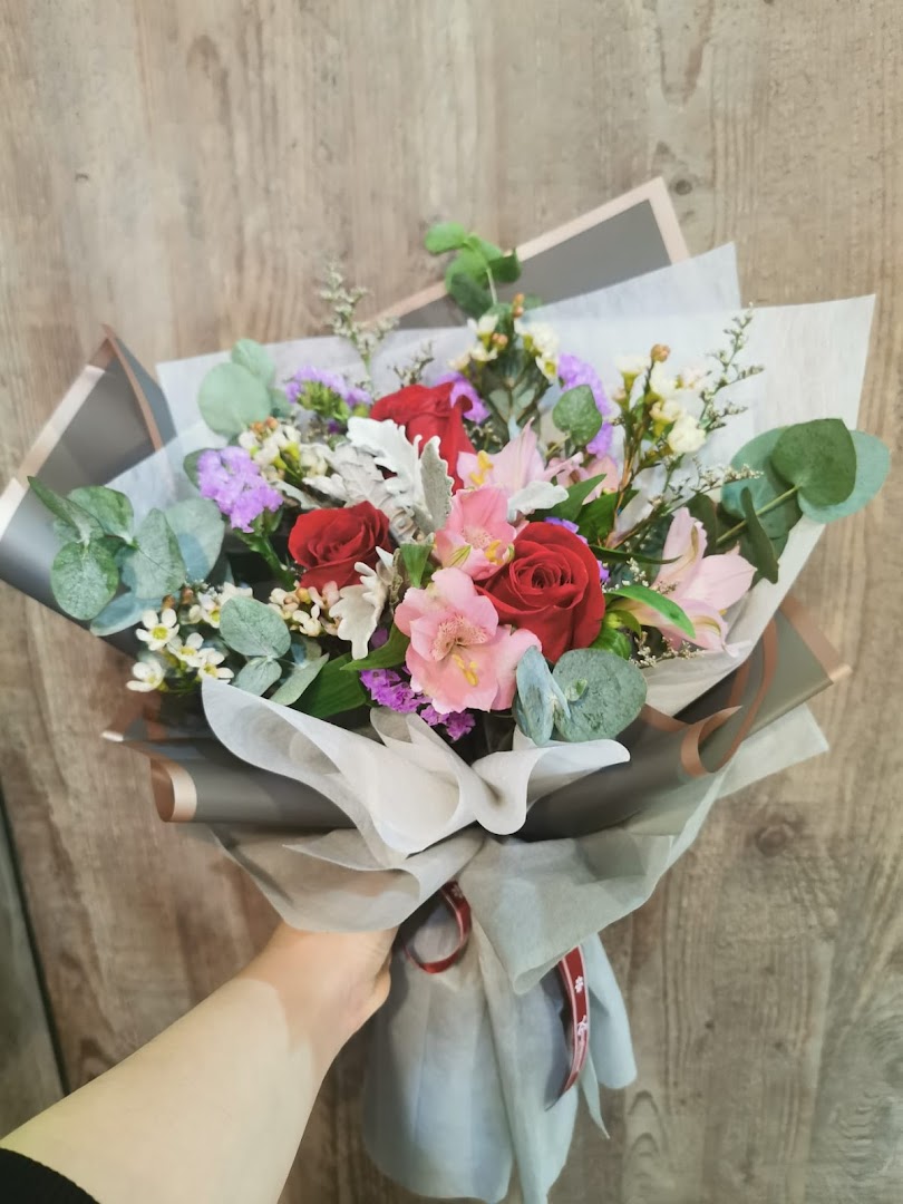 A hand holds a vibrant, beautifully wrapped floral bouquet featuring red roses and mixed blooms.