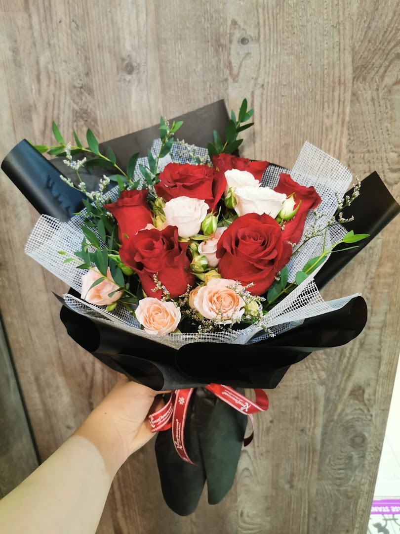 A hand holds a beautifully wrapped bouquet of red, white, and light pink roses with green foliage.