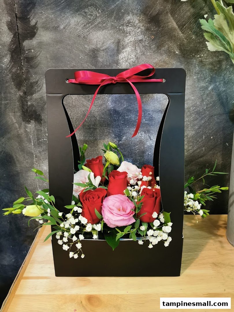 A vibrant bouquet of red and pink roses in a stylish black gift box with a red ribbon.