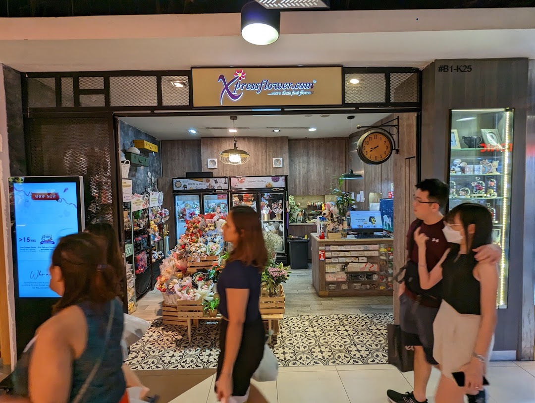 The image shows the inviting shopfront of Xpressflower, a vibrant floral and gift shop, with customers passing by.