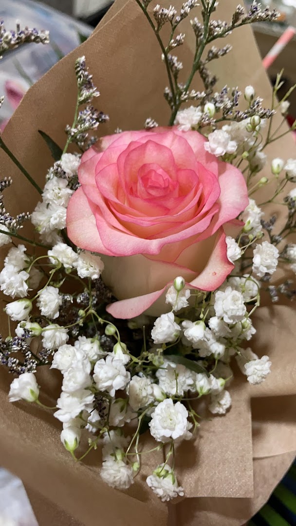 A close-up of a beautiful pink and white rose bouquet with baby's breath, wrapped in brown paper.
