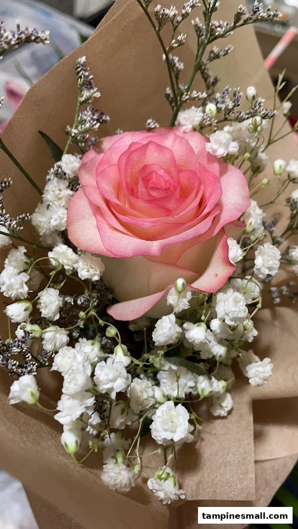 A close-up of a beautiful pink and white rose bouquet with baby's breath, wrapped in brown paper.