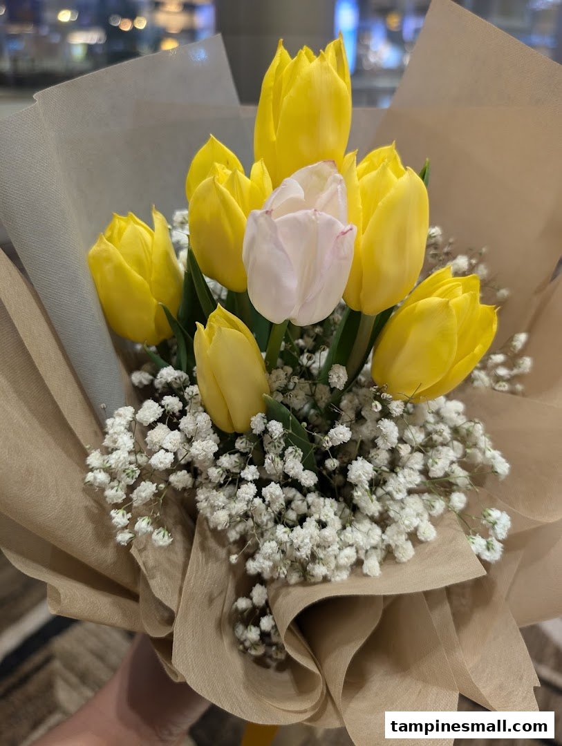 A vibrant bouquet featuring yellow and white tulips with baby's breath, wrapped in brown paper.