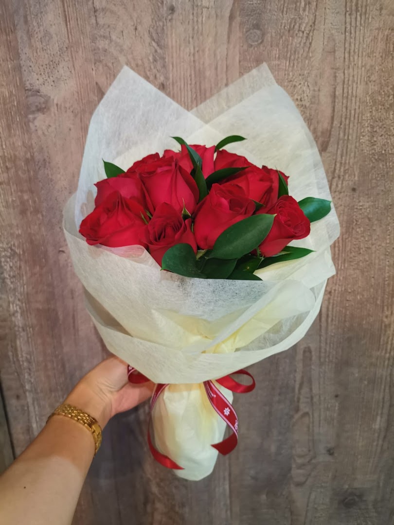 A hand holds a beautiful bouquet of vibrant red roses wrapped in delicate paper and tied with a red ribbon.