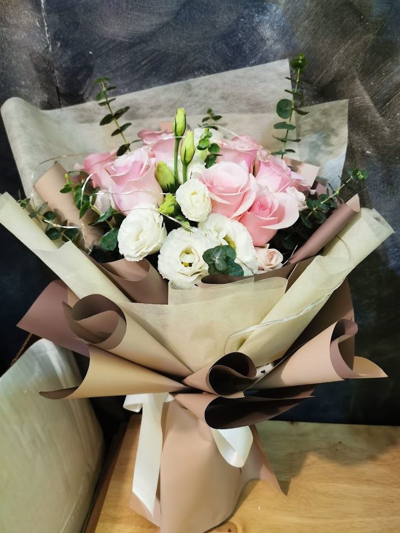 A beautifully wrapped bouquet featuring pink roses, white flowers, and subtle fairy lights.