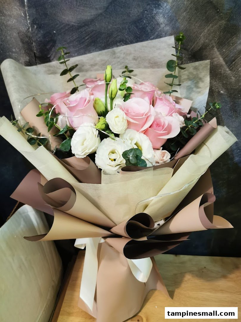 A beautifully wrapped bouquet featuring pink roses, white flowers, and subtle fairy lights.