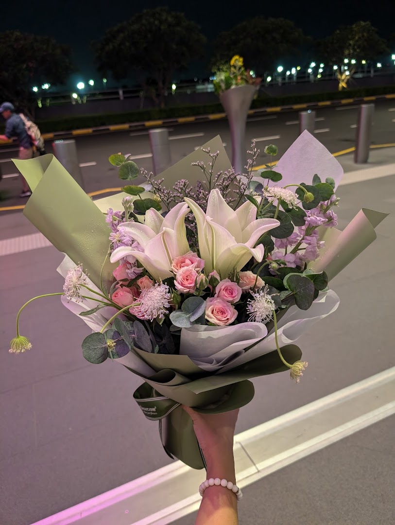 A hand holds a beautifully wrapped bouquet of fresh lilies, roses, and other flowers at night.