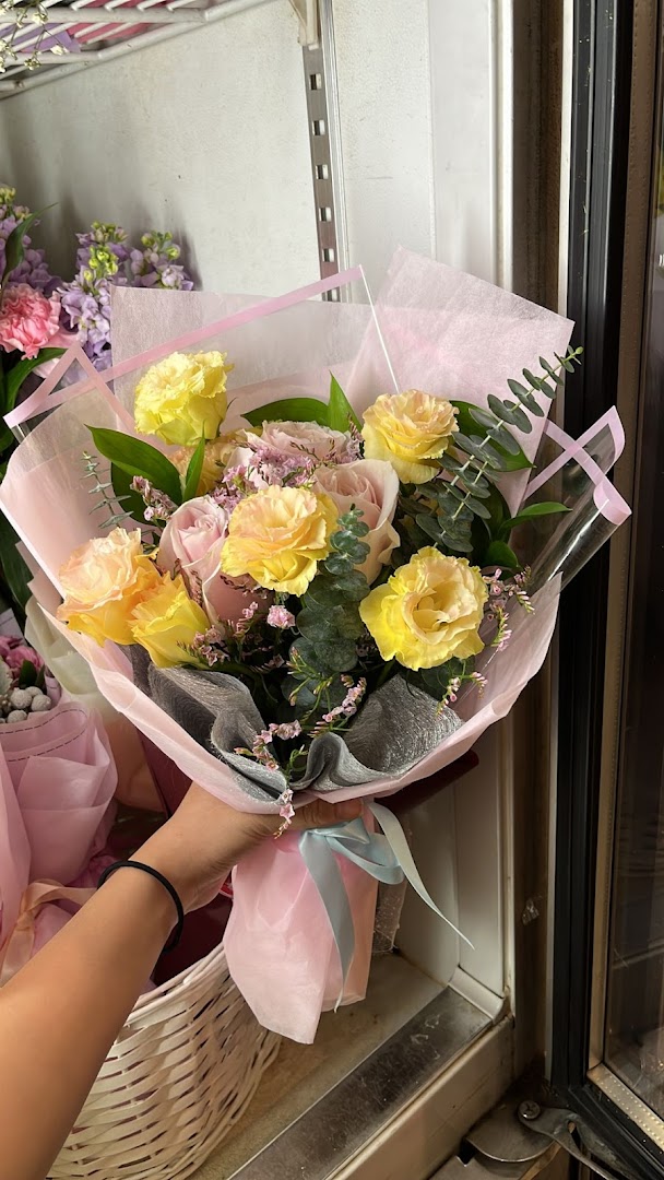A hand holds a beautifully wrapped bouquet of yellow and pink flowers with green foliage.