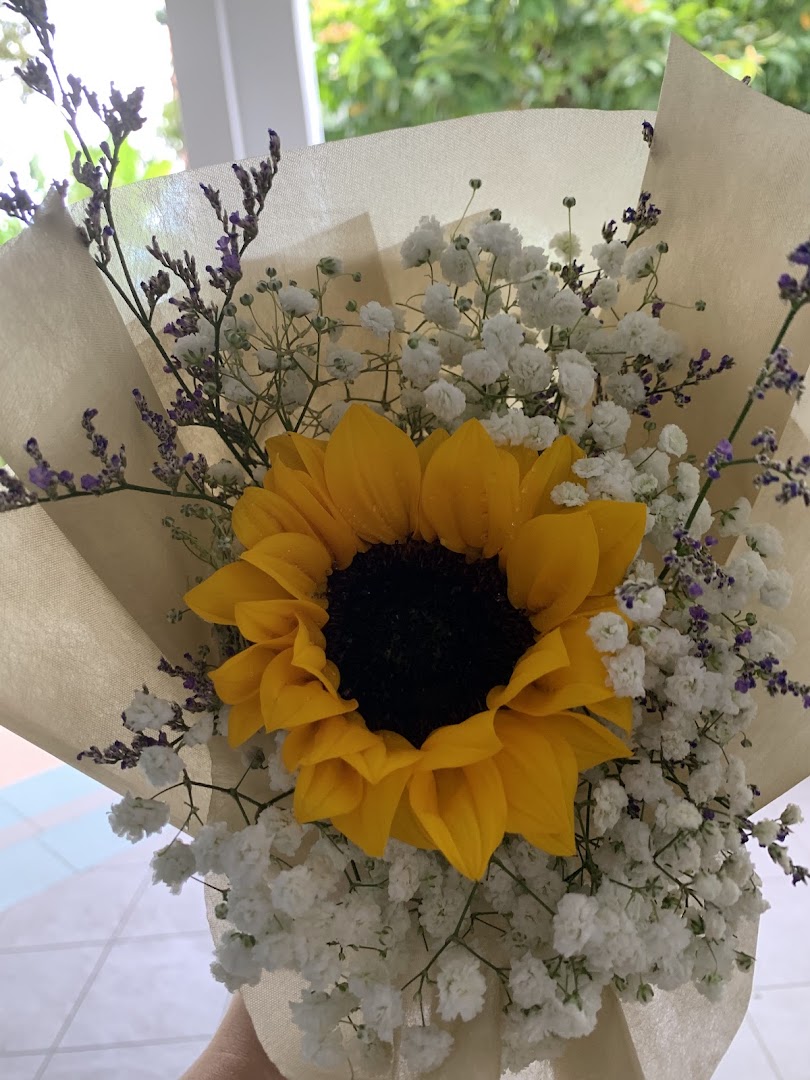 A vibrant sunflower bouquet with baby's breath and purple accents, beautifully wrapped.