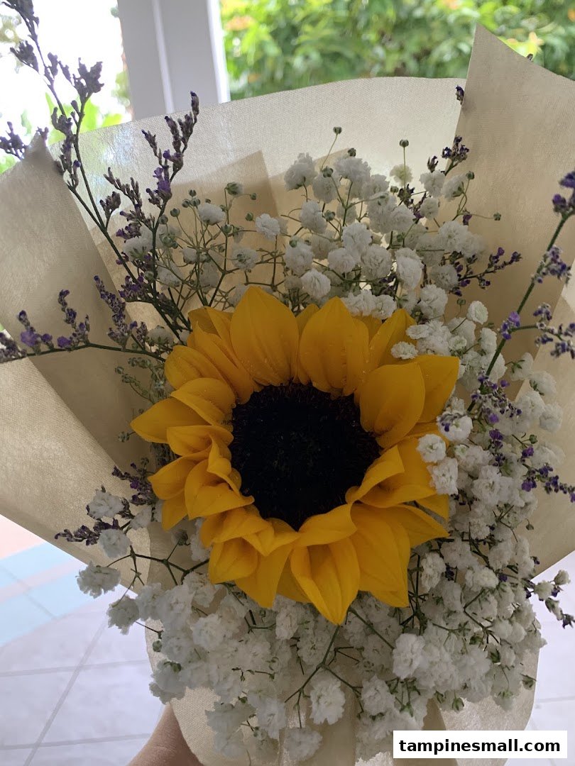 A vibrant sunflower bouquet with baby's breath and purple accents, beautifully wrapped.