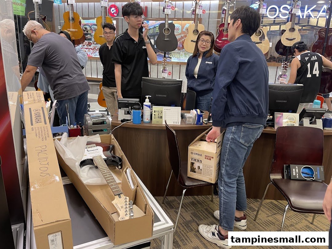 Customers and staff interact in a Yamaha Music School, surrounded by guitars, with a new electric guitar being unboxed.