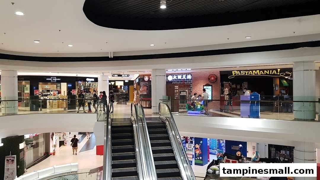 View of a multi-level shopping mall interior with various shops, escalators, and shoppers.
