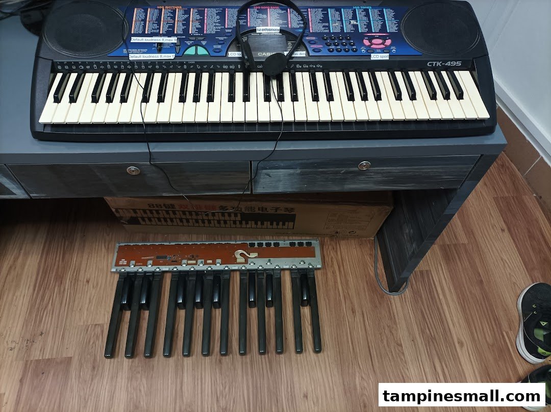 A Casio keyboard with headphones on a table, with keyboard parts and a box on the floor.