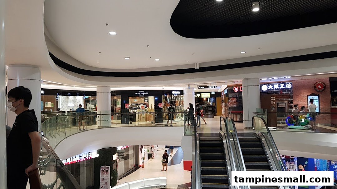 Interior view of a multi-level shopping mall with escalators and various retail shops, including Yamaha Music School.