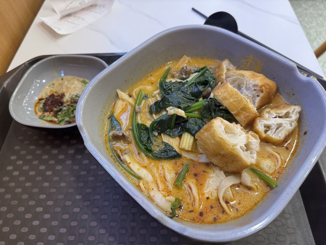 A close-up of a vibrant bowl of Mala Tang with various ingredients and a side sauce.