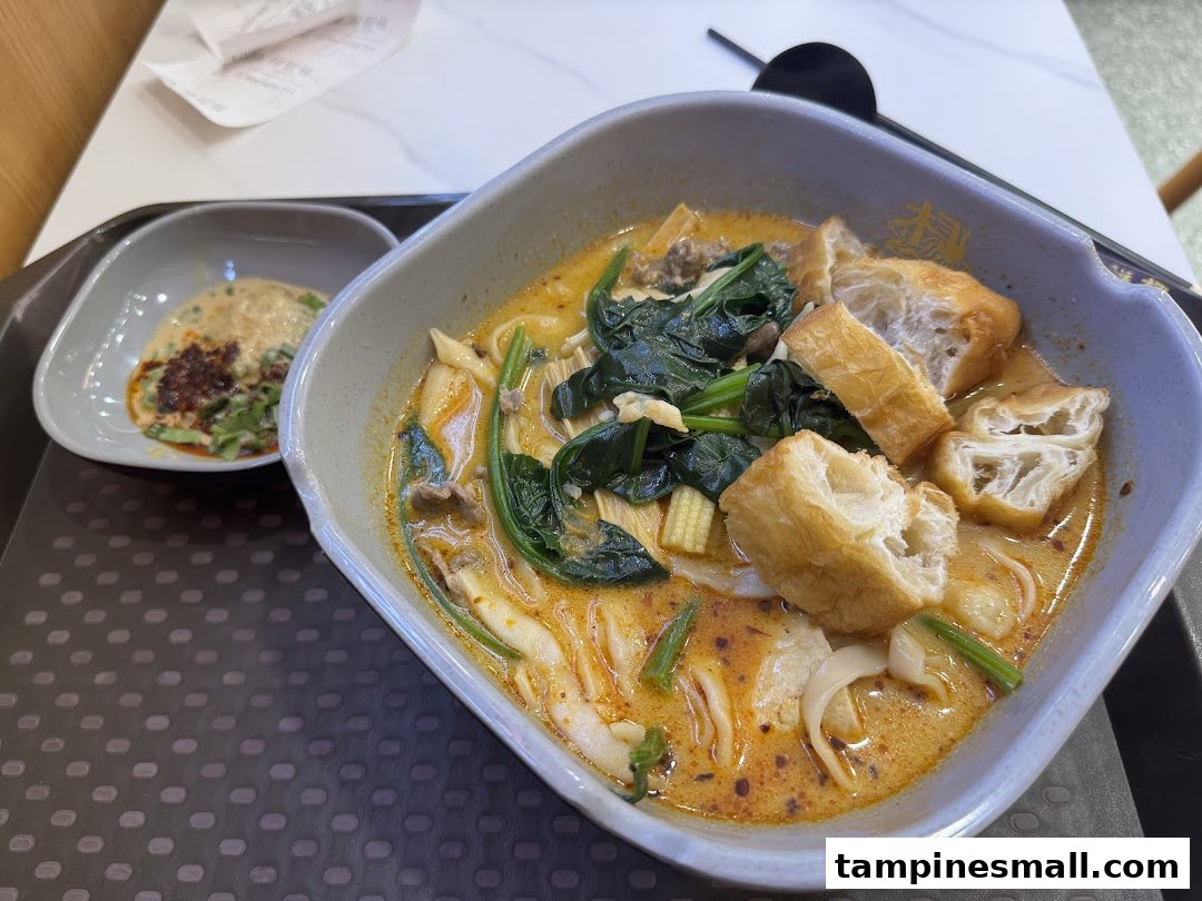 A close-up of a vibrant bowl of Mala Tang with various ingredients and a side sauce.