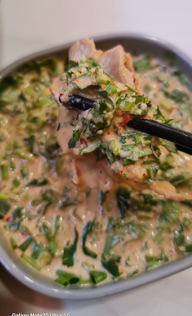 A close-up of a creamy, spicy dish with meat and fresh herbs, being lifted by chopsticks.