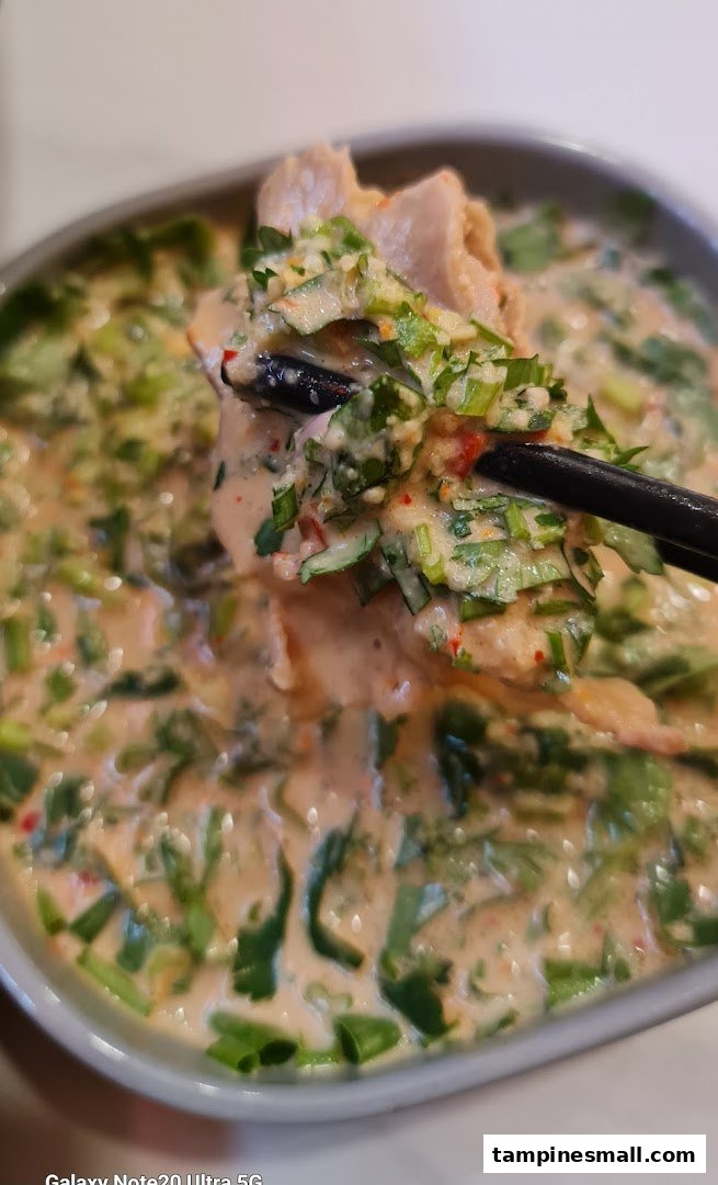 A close-up of a creamy, spicy dish with meat and fresh herbs, being lifted by chopsticks.