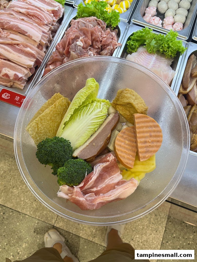 A clear bowl filled with various fresh ingredients for Mala Tang, selected from a self-serve counter.
