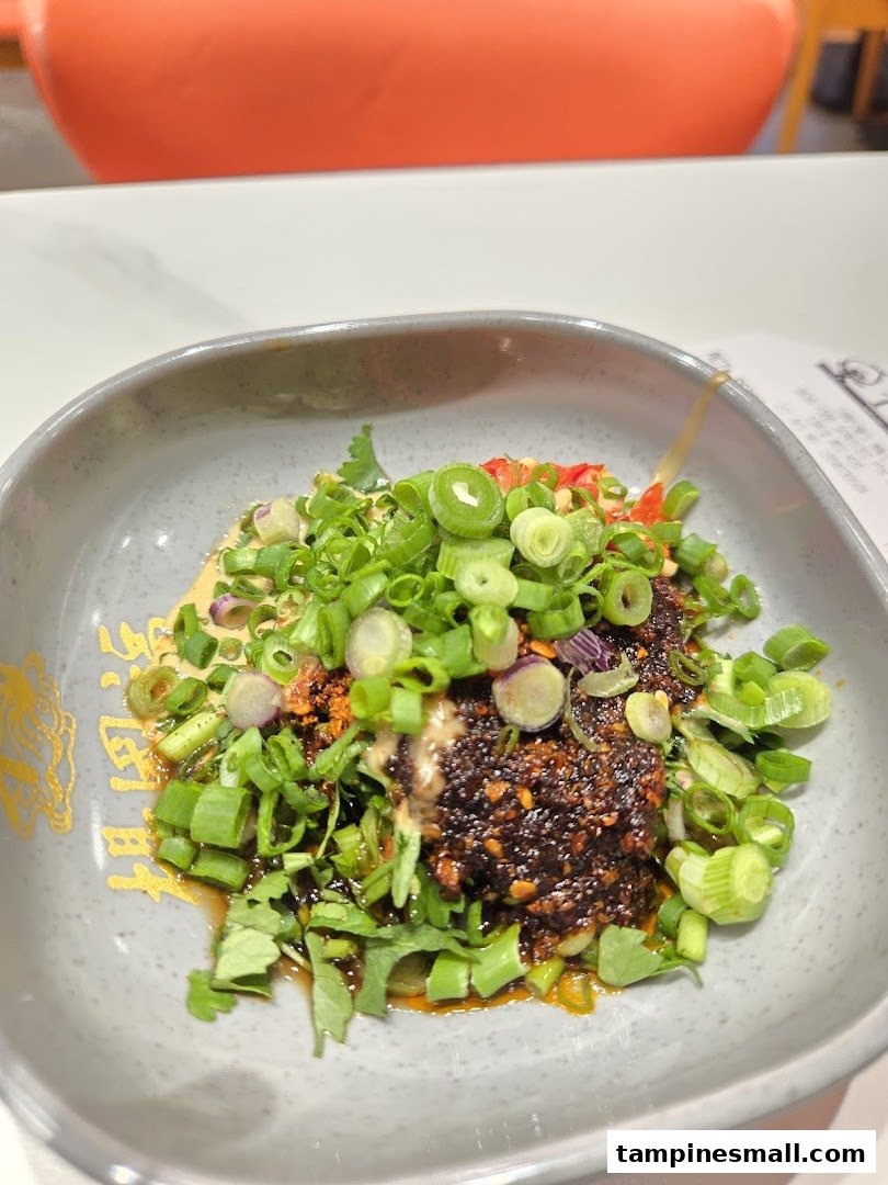 A close-up of a spicy sauce dish topped with fresh green onions and cilantro in a grey bowl.