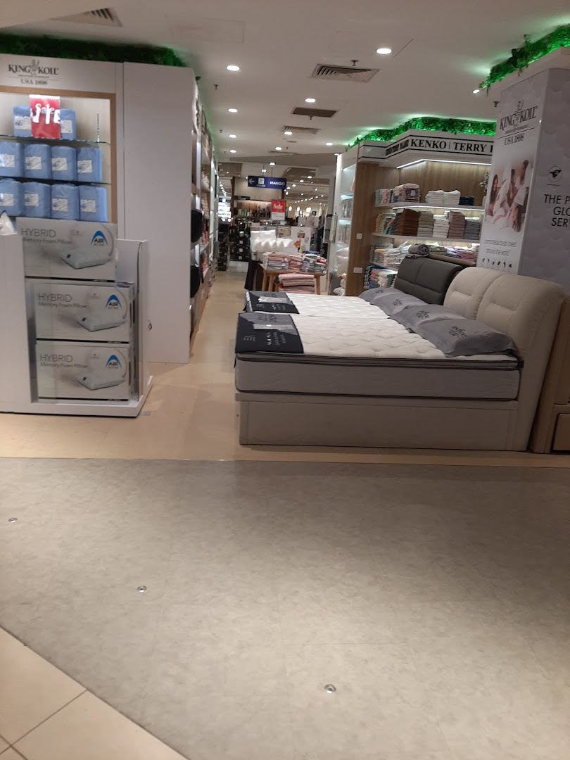 An interior view of a department store's bedding and mattress section, featuring various home comfort products.