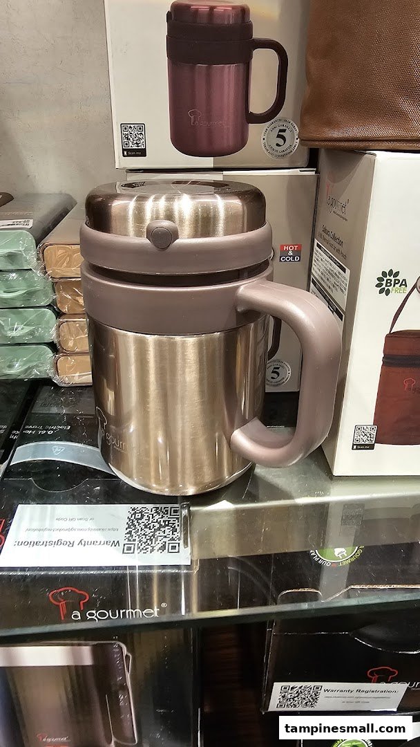 Close-up of 'a gourmet' brand thermal food jars and mugs displayed in a retail setting.