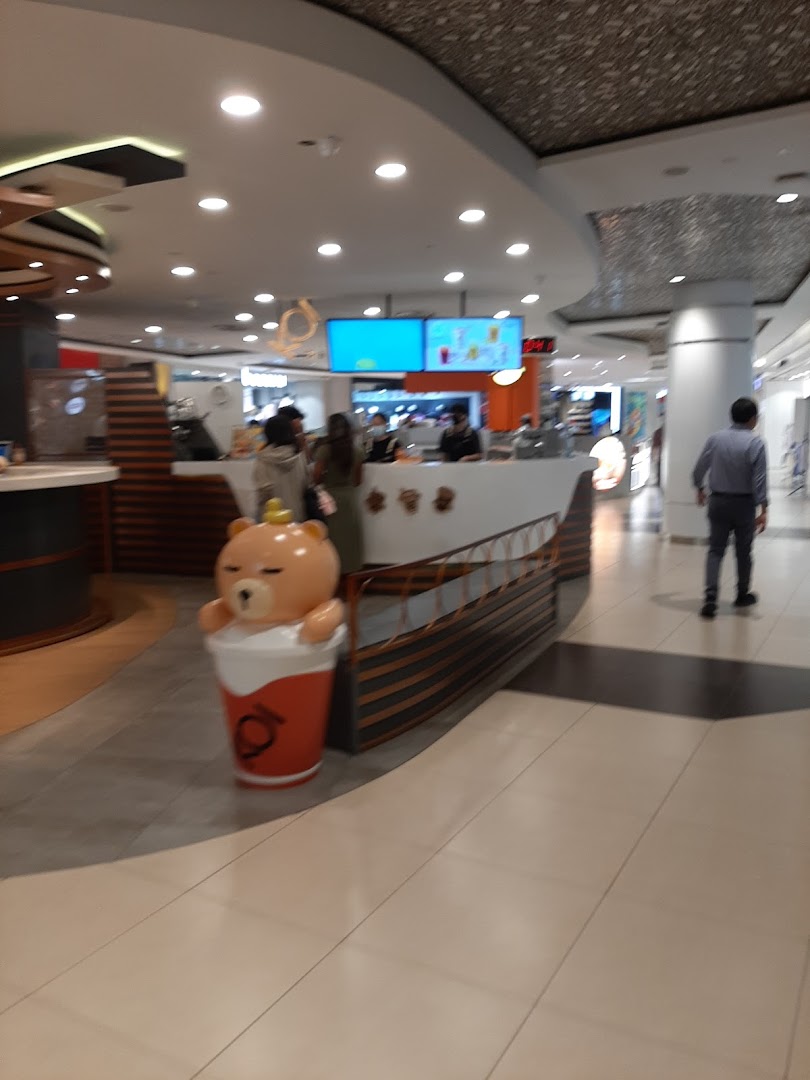 An interior view of a vibrant beverage stall featuring a large, cute bear mascot and customers.