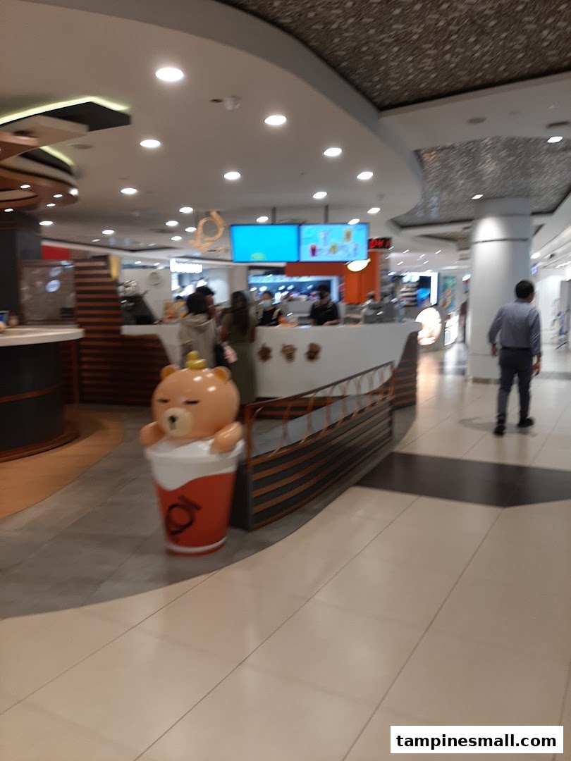 An interior view of a vibrant beverage stall featuring a large, cute bear mascot and customers.