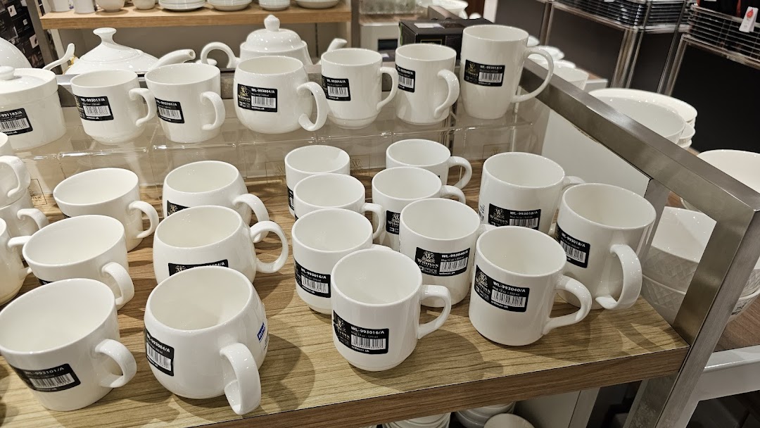 A retail display showcasing numerous white ceramic mugs and other kitchenware items on wooden shelves.