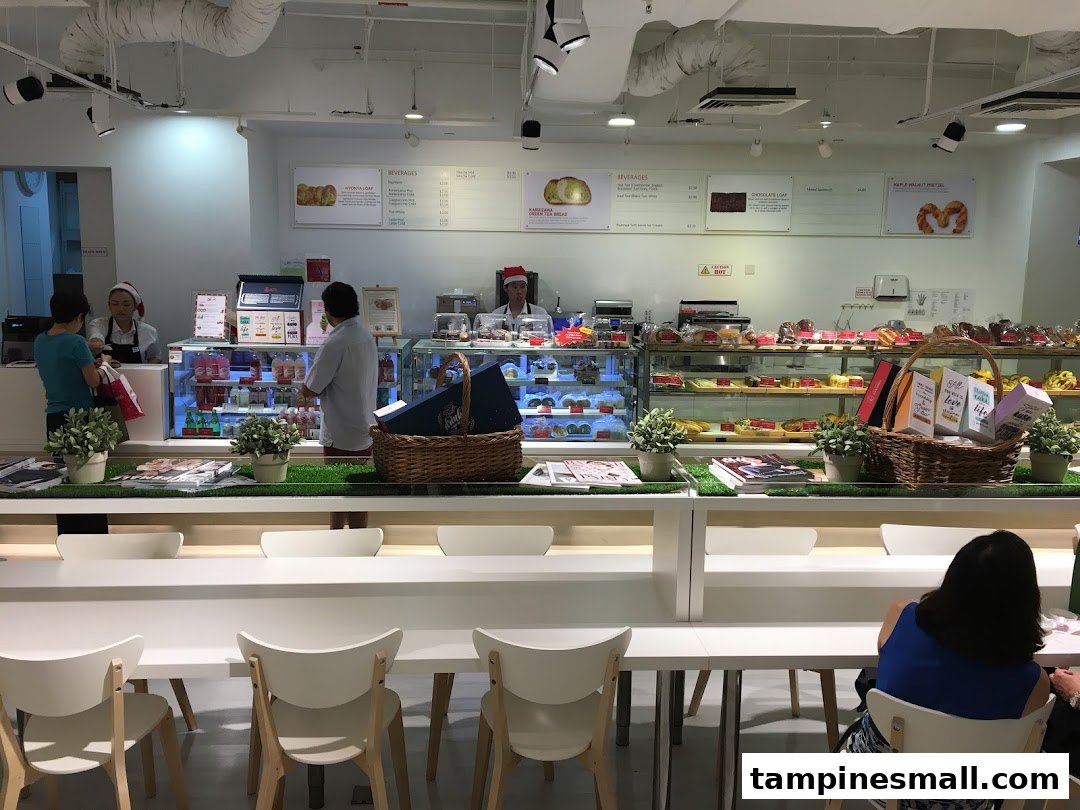 Bright interior of a modern bakery and cafe with display cases, counter, and seating.