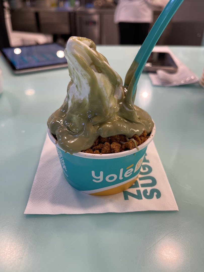 A delicious Yolé frozen yogurt with green sauce and cookie crumble toppings in a cup.
