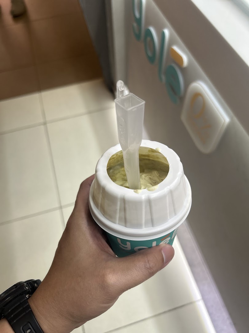 A hand holds a Yolé frozen yogurt cup with a spoon, showing the shop's branding in the background.