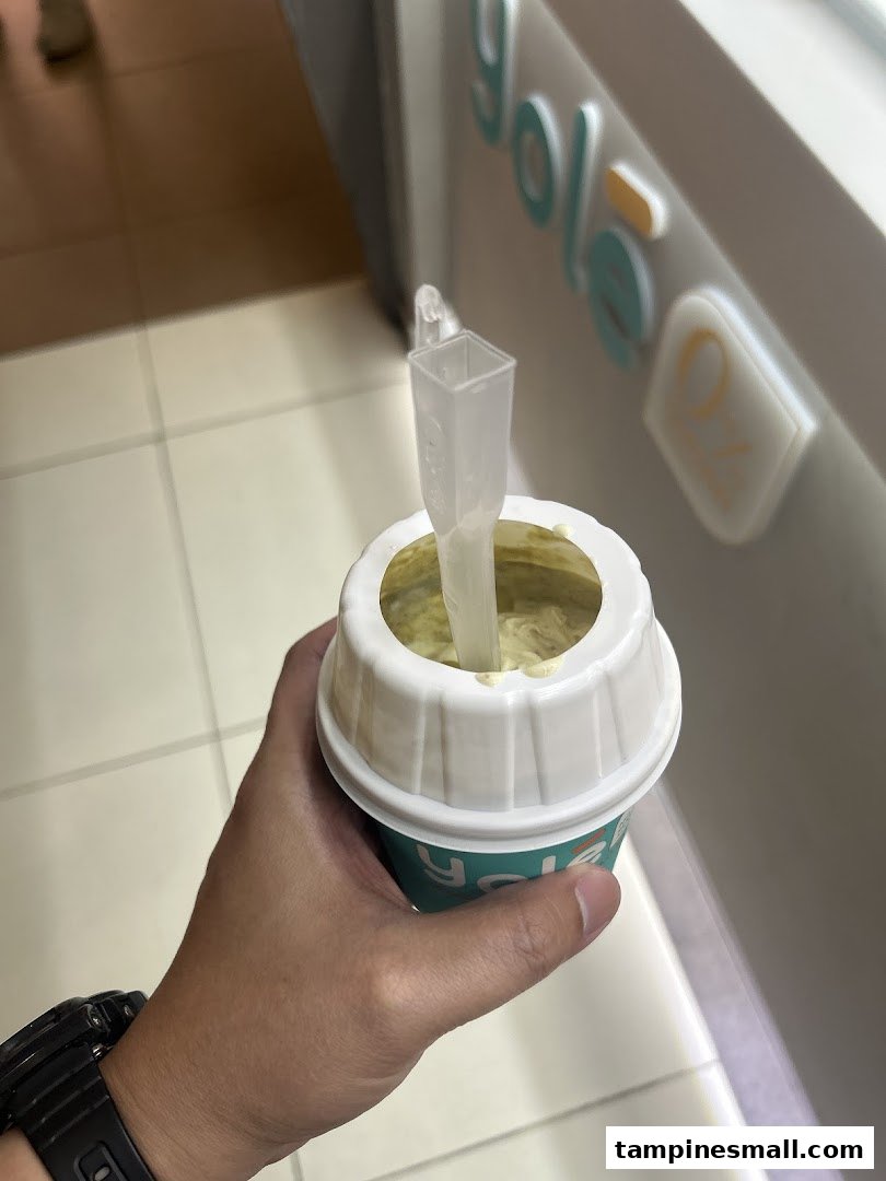 A hand holds a Yolé frozen yogurt cup with a spoon, showing the shop's branding in the background.