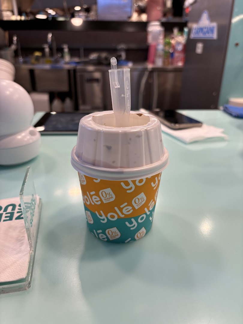 A Yolé frozen yogurt cup with a topping dispenser on a light blue counter.