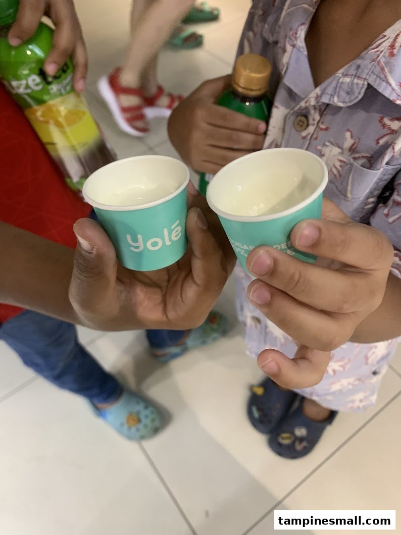 Two small Yolé cups held by children, with drinks and people in the background.