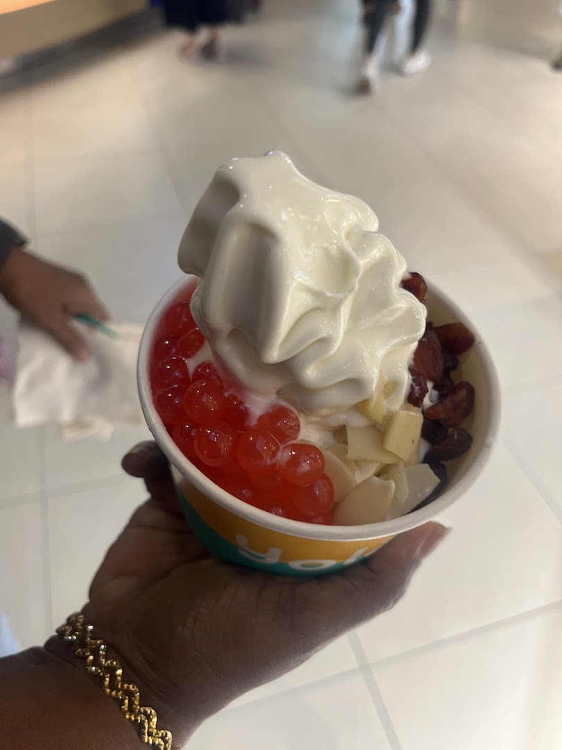 A hand holds a cup of Yolé frozen yogurt with various toppings like popping boba, dried fruit, and coconut flakes.