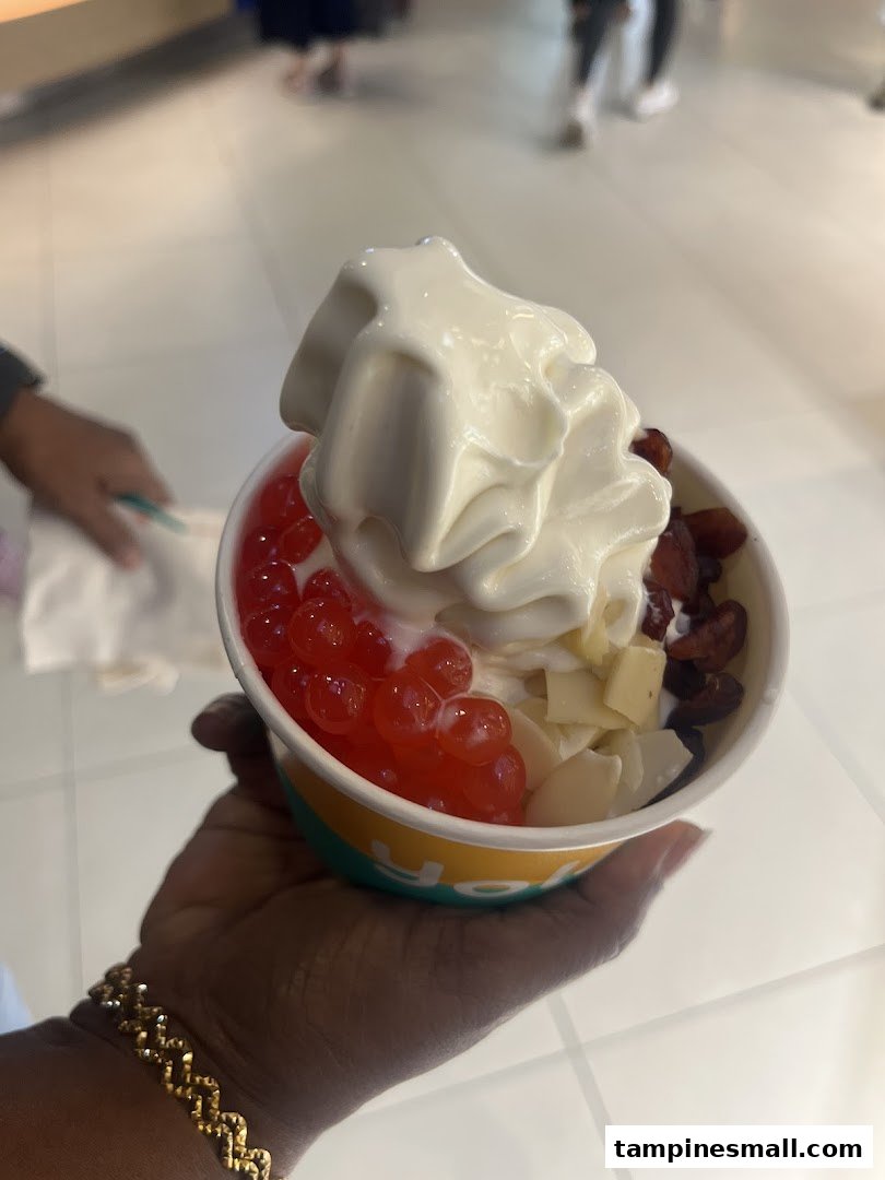 A hand holds a cup of Yolé frozen yogurt with various toppings like popping boba, dried fruit, and coconut flakes.