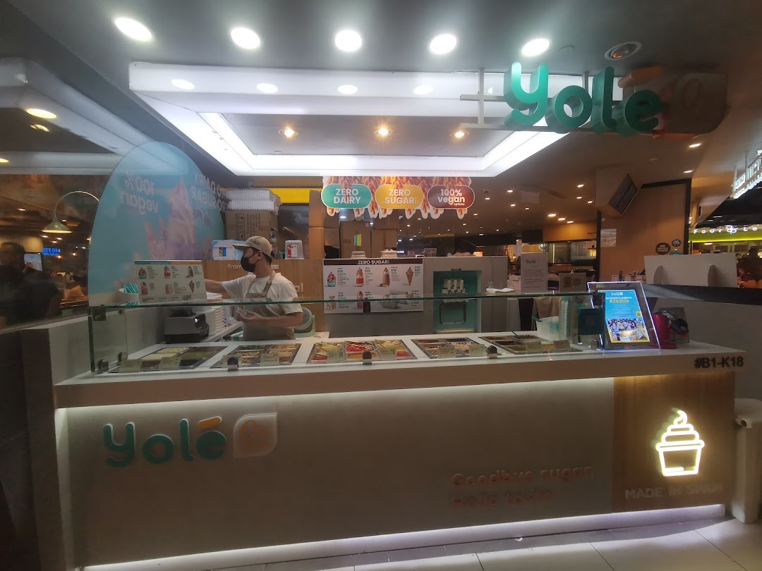 A Yolé frozen yogurt counter with an employee, showcasing healthy options like zero sugar and vegan choices.