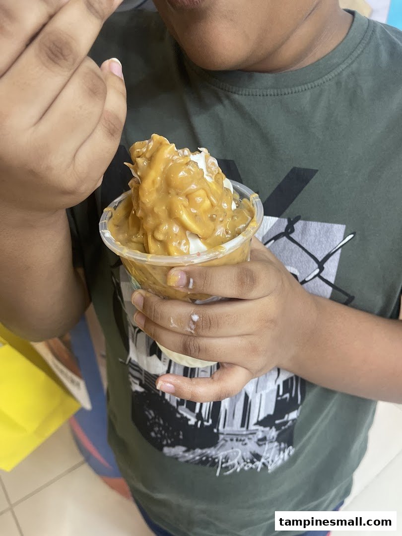 A person enjoys a delicious Yolé frozen yogurt topped with a rich, creamy sauce.