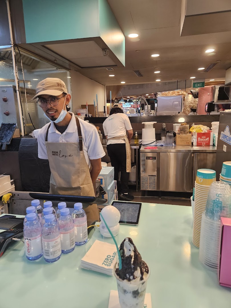 A friendly Yolé staff member at the counter, with a delicious frozen yogurt dessert ready for enjoyment.