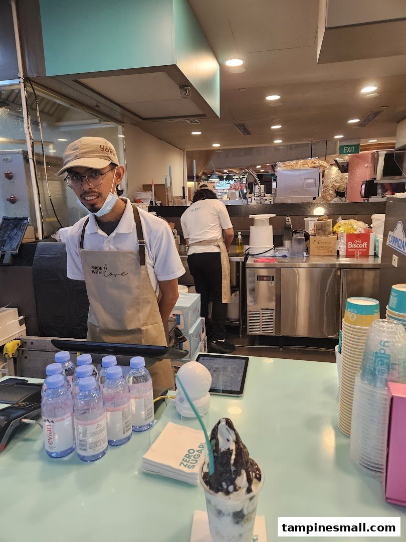 A friendly Yolé staff member at the counter, with a delicious frozen yogurt dessert ready for enjoyment.