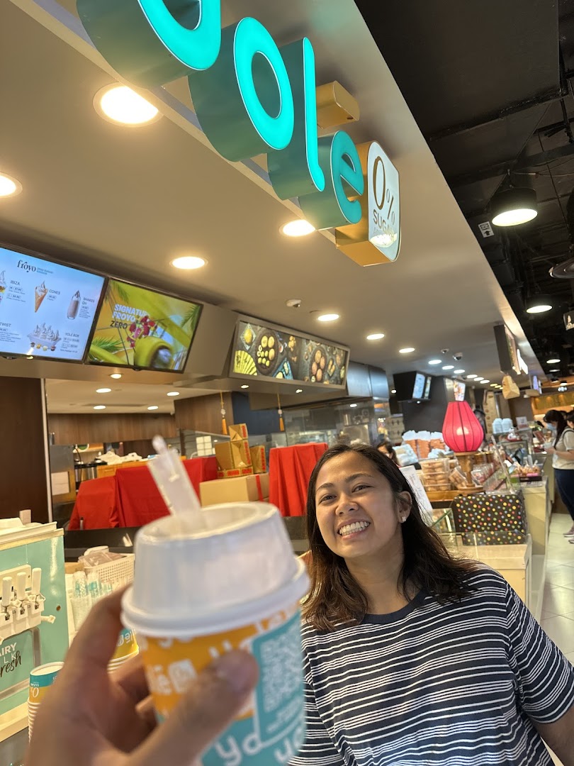 A customer holds a Yolé frozen yogurt cup inside the shop, with the brand's signage visible.