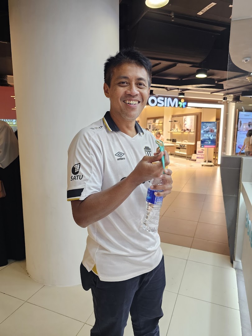 A smiling man holding a water bottle in a mall corridor, with an OSIM store in the background.
