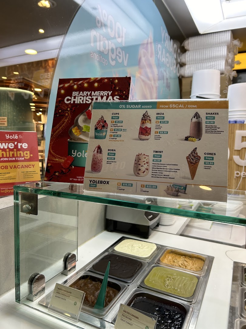 A Yolé frozen yogurt counter displaying a detailed menu board with various froyo options, shakes, and toppings.