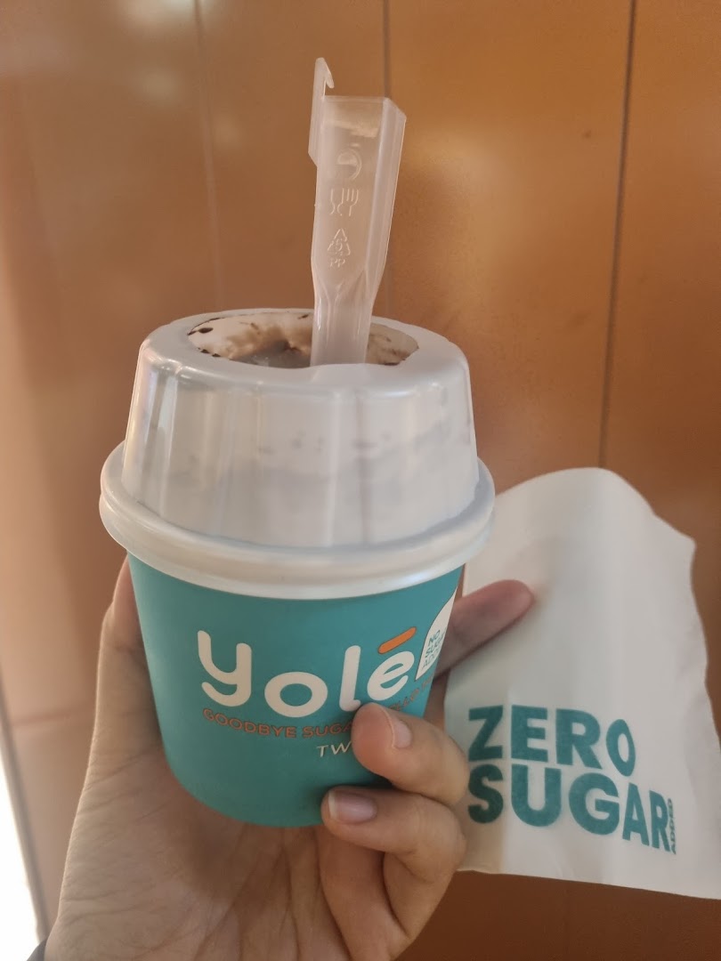 A hand holding a Yolé frozen yogurt cup with a 'Zero Sugar' napkin.