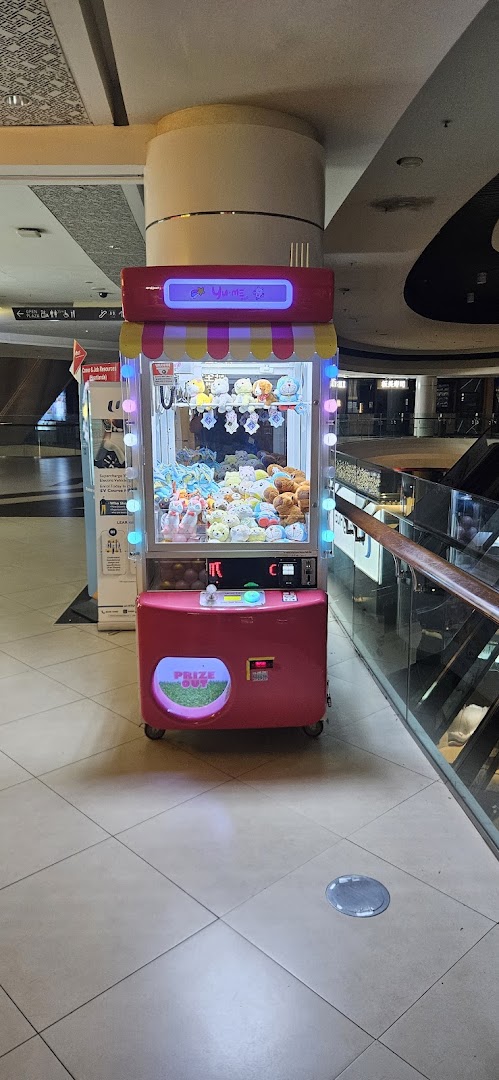 A vibrant pink Yume Claw machine filled with various plush toys stands in a mall corridor.