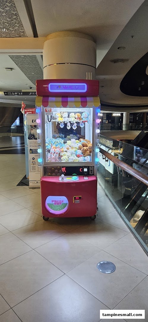 A vibrant pink Yume Claw machine filled with various plush toys stands in a mall corridor.