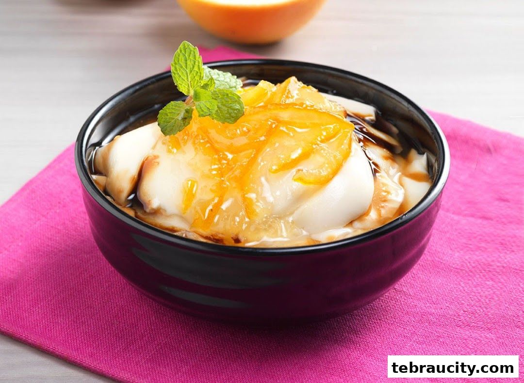 A close-up of a dessert bowl filled with creamy tofu pudding topped with orange preserves and mint.