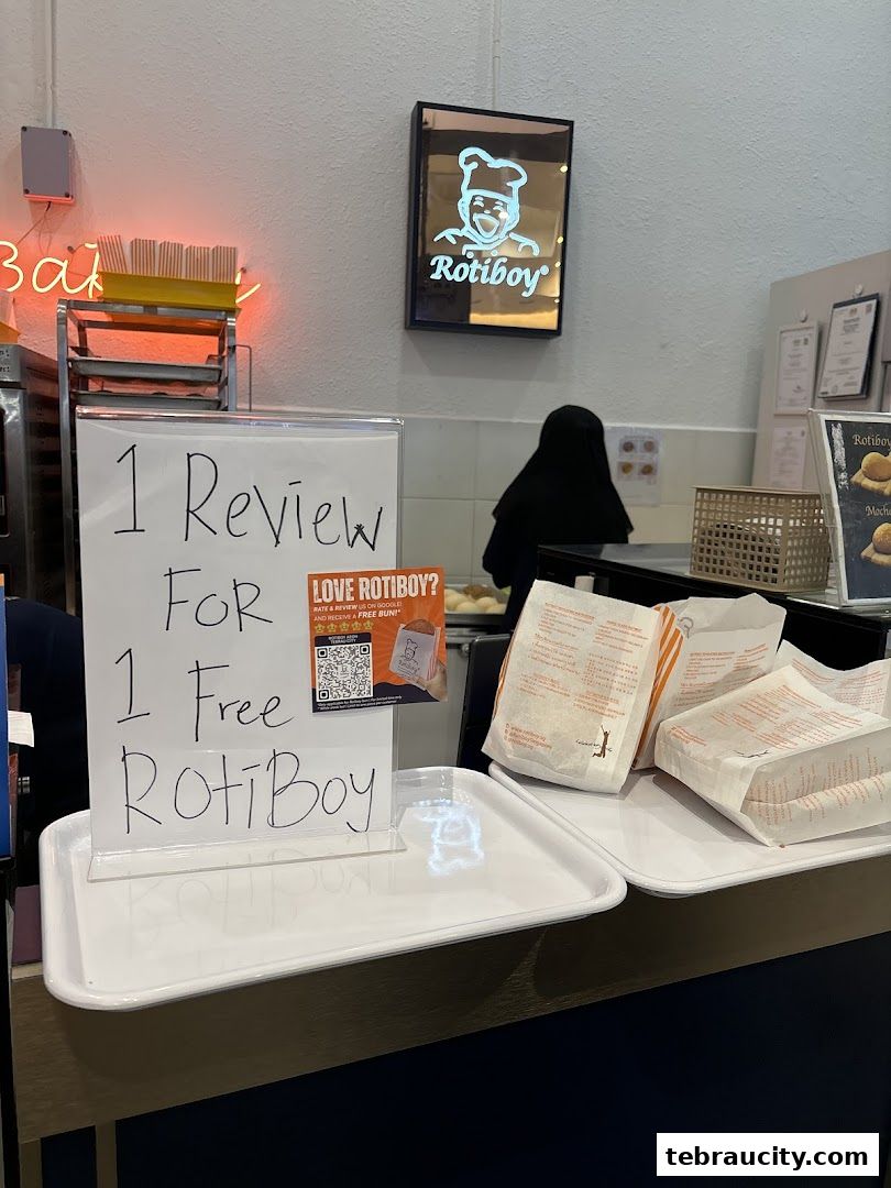 A sign offering a free RotiBoy bun for one review, with RotiBoy branded packaging visible.
