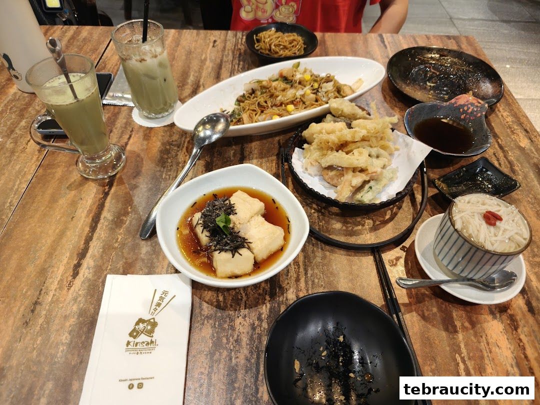 A table laden with various Japanese dishes and drinks, including tempura and iced beverages.
